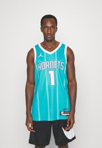 Teal basketballtrøje med "HORNETS" og nummer "1" i lilla. Har hvide striber og rund halsudskæring, parret med sorte shorts.