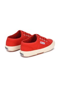 Sneakers in tela rossa con design a profilo basso, chiusura con lacci e suole in gomma beige caratterizzate da motivi testurizzati e branding sulla linguetta.