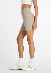 Shorts beiges tailles hautes avec texture côtelée, longueur mi-cuisse. Associés à des chaussures de sport blanches et des chaussettes avec un logo.