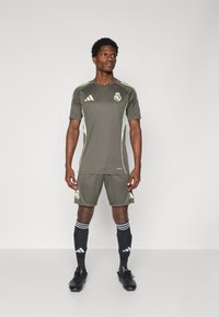 Uniforme de fútbol en tono verde grisáceo con mangas cortas, que presenta acentos en verde claro, logotipo del club y calcetas negras con rayas blancas. Botas negras.