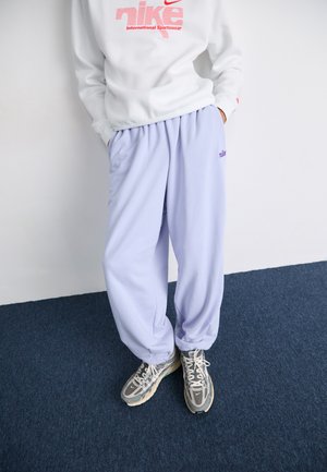 Pantalons de survêtement violet clair avec poches latérales et logo "nike" brodé. Assortis à des baskets grises avec des lacets blancs et un design texturé.