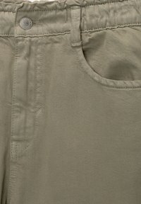 Pantalons kaki en tissu texturé, avec une taille élastique et une poche avant. Détail de couture notable le long des coutures.