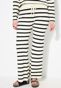 Gestreepte loungebroeken van crème en zwarte gebreide stof, met een trekkoord in de taille en een uitlopende snit voor comfort en bewegingsgemak.