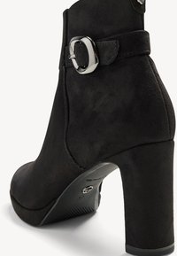 Svart mocka ankstövel med rund tå, hög klack och en metallisk spänne som accent på sidan. Slät textur med en åtsittande design.