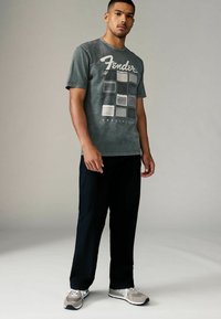 Gray cotton t-shirt featuring a Fender amplifier graphic in white and gray, paired with black pants and gray sneakers.
