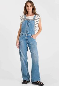 Lichtblauwe denim tuinbroek met verstelbare bandjes, knoopsluiting aan de voorkant en wijde pijpen. Gecombineerd met een gestreept topje met korte mouwen.