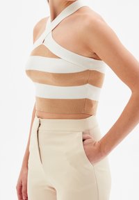Top corto de punto a rayas beige y blanco con diseño de cuello halter. La tela es suave, con forma ajustada y una textura lisa.
