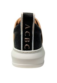 Sneaker in suede nero con suola bianca, caratterizzato da un tallone in pelle color cuoio. La parte posteriore presenta un logo dorato e accenti a righe bianche.