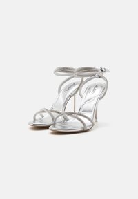 Sølv høyhælte sandaler med en glatt metallisk finish, med kryssremmer prydet med glitrende detaljer og en ankelrem.
