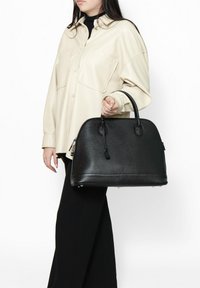 Borsa in pelle nera dalla forma rotonda, con finitura texture e manici corti. Dettagli notevoli includono una tracolla removibile e accenti metallici.