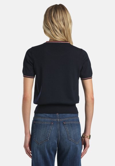 Tengerészkék rövid ujjú kötött felső testhez simuló szabással. Piros-fehér csíkos gallérral és bordázott szegéllyel rendelkezik. Farmernadrággal párosítva.