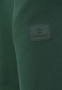 Πράσινο φούτερ με λεία υφή, που διαθέτει ένα ορθογώνιο σκούρου πράσινου χρώματος έμβλημα της Timberland στο μπροστινό μέρος.