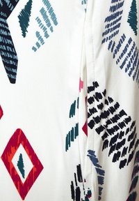 Tissu à motifs blanc, présentant des formes géométriques en sarcelle, marine, rouge et noir. Texture lisse avec des styles de lignes variés et des accents.