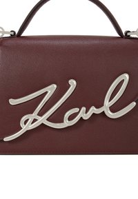Burgundy leather handbag featuring a prominent silver logo, structured shape, and a top handle for carrying. Smooth texture with stitching details.