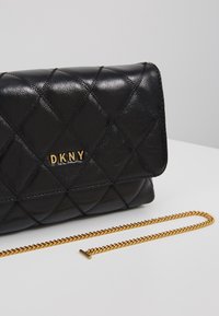 Černá prošívaná kožená psaníčko se zlatým řetízkem, s zlatým logem "DKNY" a elegantním obdélníkovým designem.