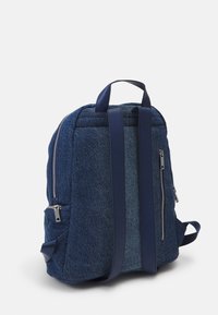 Niebieski plecak dżinsowy o teksturowanym wykończeniu, z dwiema zamykanymi na zamek bocznymi kieszeniami, materiałowymi paskami oraz gładką, skórzaną rączką.