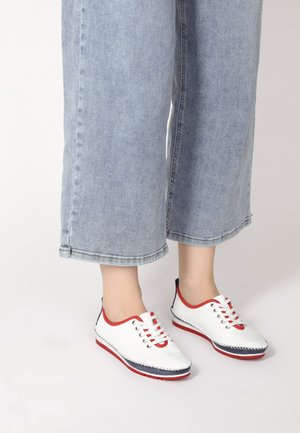 Weiße Schuhe mit roten Akzenten und Schnürsenkeln, ausgestattet mit navyblauen Verstärkungen und sichtbaren Nähten, kombiniert mit hellblauen, gekürzten Jeanshosen.
