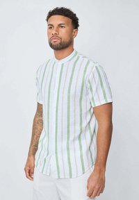 Chemise à manches courtes blanche avec des rayures verticales vertes et beiges. Dotée d'un col mandarin et d'une fermeture à boutons sur le devant. Tissu texturé.