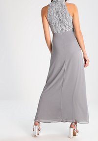Gray halter neck dress with a patterned top, flowing skirt, and intricate detailing. Features ankle strap heels with a metallic finish.
