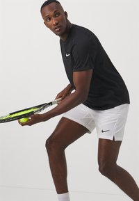 Zwarte Nike sportshirt en witte shorts. Het shirt heeft korte mouwen en een ronde hals; de shorts hebben twee zijzakken en een split aan de zoom.