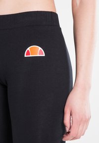 Sorte tights med en myk tekstur, med en hvit logo i oransje og røde nyanser på den øvre siden. Elastisk midje for komfort.