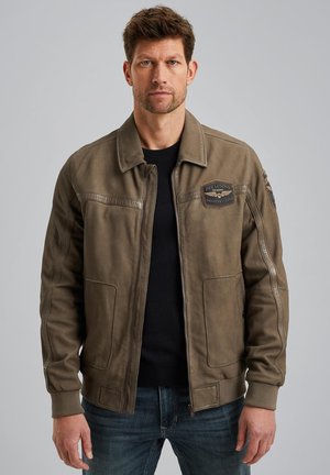 Veste bomber en cuir vert olive avec des poignets et un ourlet côtelés, des détails de patch sur la poitrine et des poches latérales, assortie à un jean foncé.