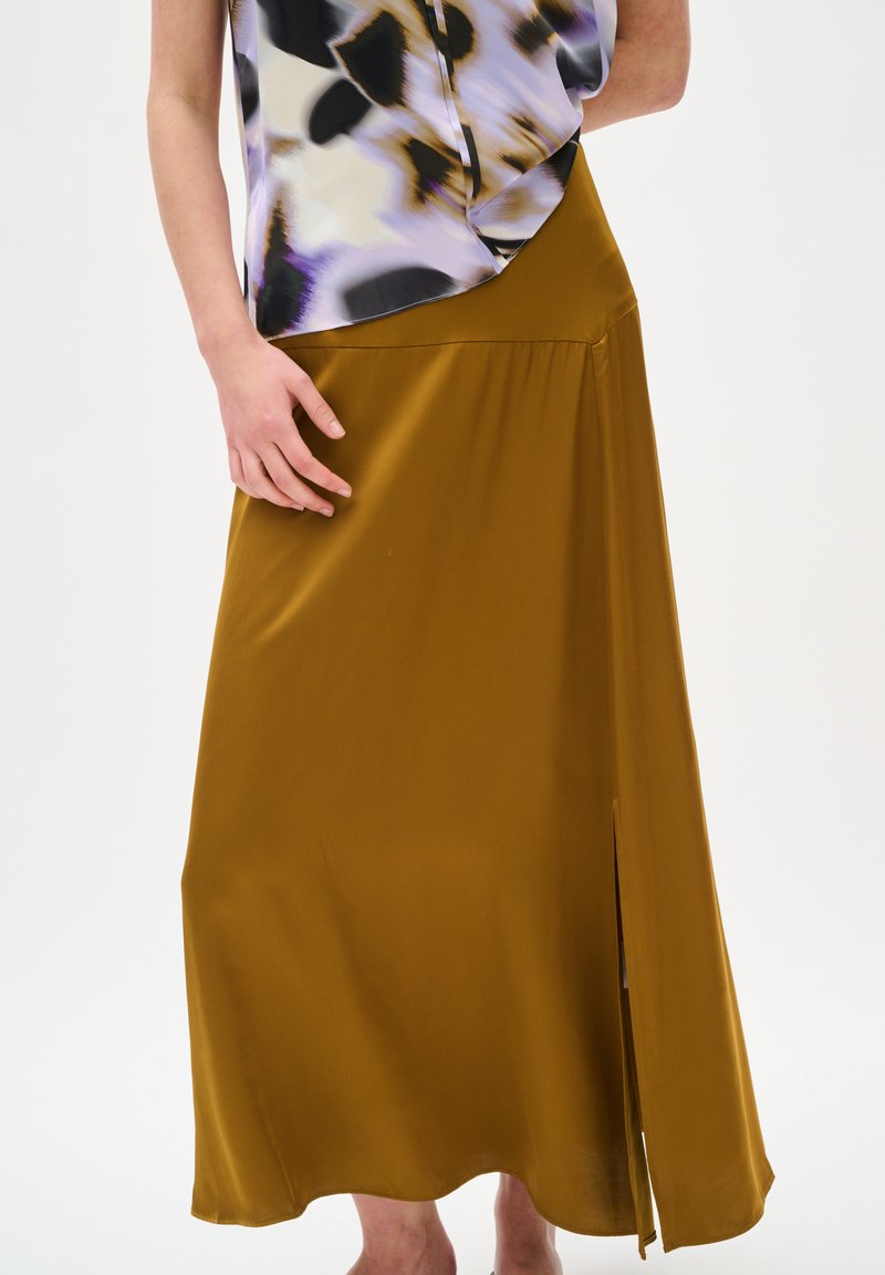 Jupe en satin couleur moutarde avec une fente sur le côté, au design fluide, à la légère brillance et à la texture douce. Accompagnée d'un chemisier à motifs.