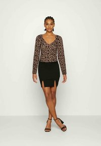 Camisola de mangas longas em castanho com padrão floral preto; combinada com uma saia preta com uma abertura frontal. Sandálias pretas com tiras completam o look.