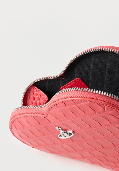 Πορτοφόλι σε σχήμα καρδιάς από δερματίνη κοραλί με υφή, ασημένιο φερμουάρ μερικώς ανοιχτό, που αποκαλύπτει εσωτερικό από μαύρο ύφασμα και κόκκινη κάρτα μέσα.