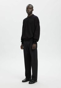 Czarna koszulka polo z długim rękawem, dwoma guzikami i luźnym krojem, w połączeniu z czarnymi spodniami o szerokich nogawkach i czarnymi butami. Gładka tekstura.