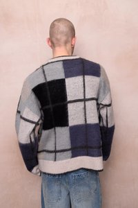 Pulover tricotat în gri, negru și bleumarin, cu un model în carouri. Are o margine și manșete ribbate, și o croială lejeră.