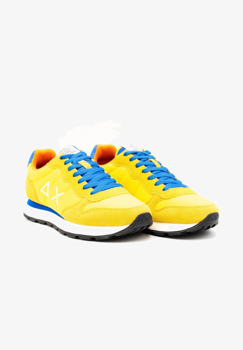 Žluté sportovní tenisky s modrými tkaničkami, svrchní materiál z semiše a síťoviny, bílá mezipodešev a černá gumová podrážka. Na boku je umístěno logo.