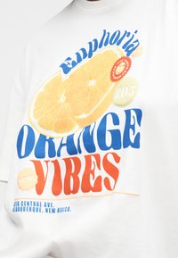 Λευκό πουκάμισο με γραφικό που απεικονίζει μια φέτα πορτοκαλιού και κείμενο «Euphoria Orange Vibes» με μπλε και πορτοκαλί γράμματα, με λεπτομέρειες πόλης από κάτω.