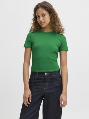 Tricou verde cu mâneci scurte, ajustat, fabricat dintr-un material moale, asortat cu blugi de denim închis cu talie înaltă, având cusături vizibile și buzunare frontale.