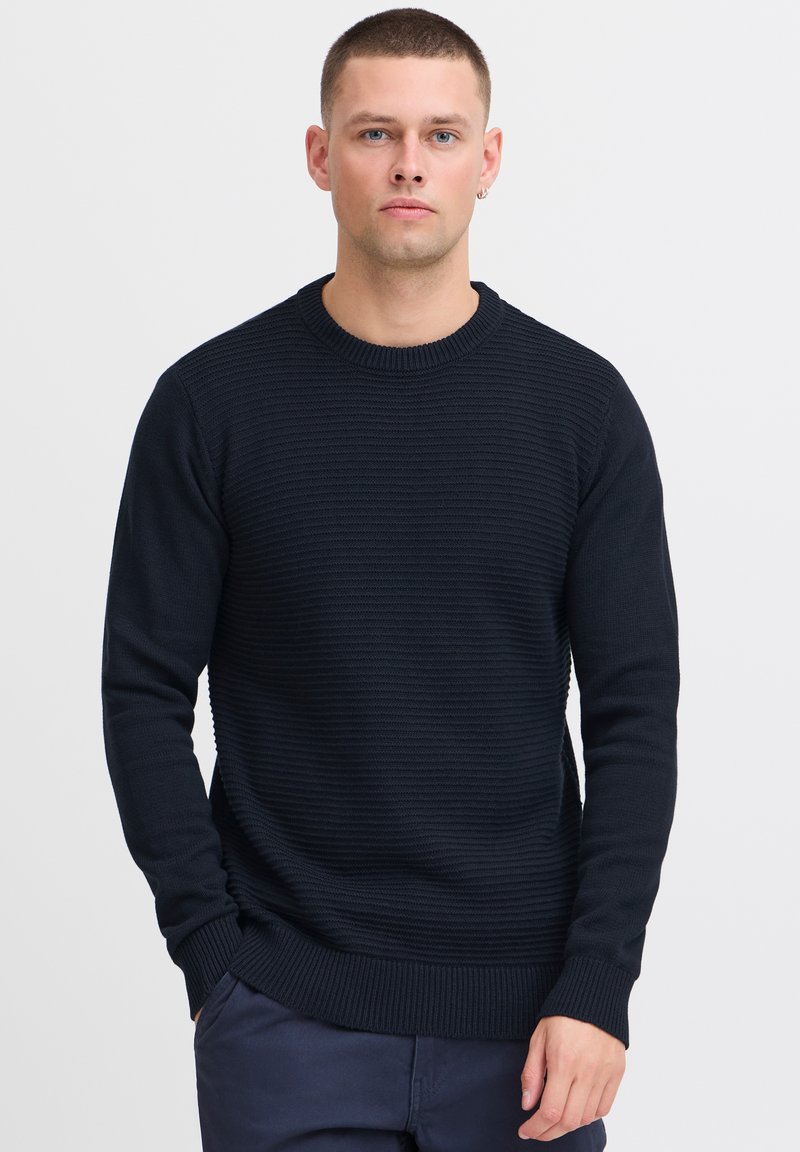 Marineblauwe ribgebreide trui met een ronde halslijn en lange mouwen. Beschikt over een textuurdesign en een fitted tailleband.
