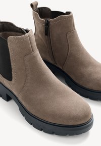 Botine din suede maro cu panouri laterale elastice negre, vârf rotunjit și talpă din cauciuc negru rezistentă. Dispune de fermoare și detalii cusute.