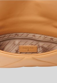 Interno di una borsa in pelle color cuoio con una tasca con zip. La fodera presenta un motivo e l'etichetta del marchio "PATRIZIA PEPE" in pelle cuoio embossata.
