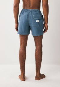 Muške kupaće gaće u prigušenoj plavoj boji, s elastičnim pojasom, stražnjim džepom s poklopcem i glatkim, laganim tkaninom.