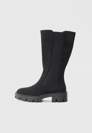 Knee-high black boots with a suede finish, elastic panels, and a thick ridged sole for grip. Simple design with a rounded toe.