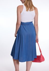 Jupe midi en denim bleu avec une silhouette fluide, dotée d'une taille et de poches, associée à un sac à main rouge pour le contraste.