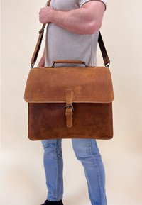 Bruine leren schoudertas met klep sluiting, verstelbare schouderband en een gesp detail. Heeft een gladde textuur en gestikte randen.