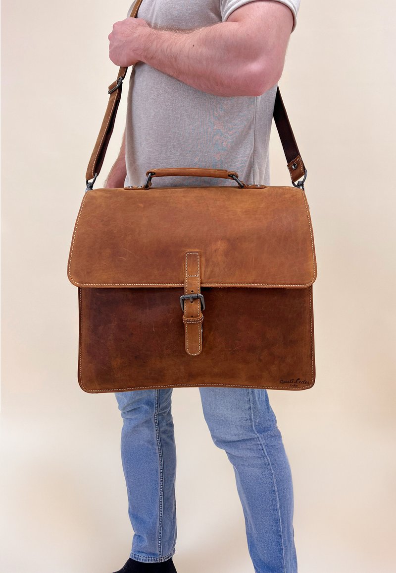 Bruine leren schoudertas met klep sluiting, verstelbare schouderband en een gesp detail. Heeft een gladde textuur en gestikte randen.