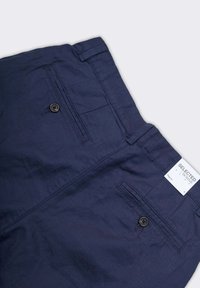 Chinos in cotone blu navy con due tasche posteriori e un piccolo bottone marrone. L'etichetta riporta 'SELECTED HOMME' con la taglia indicata come 'S'.