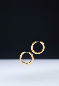 Orecchini a cerchio in oro con un design liscio e arrotondato, caratterizzati da una finitura lucida e una chiusura sicura, sospesi su uno sfondo scuro.