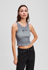 Siva rebrasta kratka majica s okruglim izrezom, s crnim natpisom "KARL LAGERFELD JEANS". Uparena s crnim trapericama visoka struka.