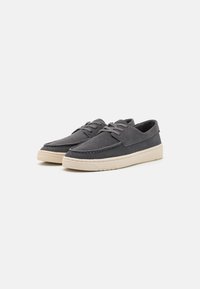 Scarpe in suede grigio con un profilo basso, caratterizzate da una suola in gomma beige e lacci. Dettagli cuciti lungo la parte superiore aggiungono consistenza e interesse.