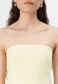Yellow strapless top featuring a smooth texture and seam detailing, paired with metallic hoop earrings.
