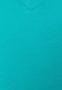 Maglietta a v blu teal realizzata in morbido cotone; presenta un design semplice e senza decorazioni con un colletto pulito e una consistenza morbida.