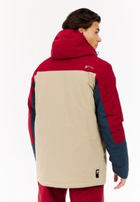 Rote, beige und marineblaue isolierte Jacke mit Kapuze; hat ein Logo auf der Rückseite; glatte Textur mit kontrastierenden Farbbereichen.