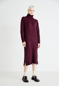 Burgundy knit turtleneck dress with long sleeves and side slits, paired with black and burgundy shoes, and cream ribbed socks.
